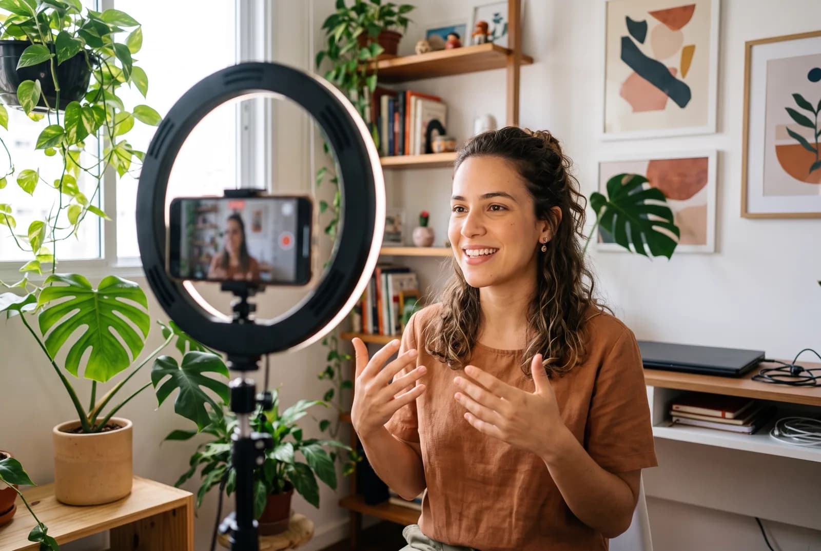 Criadora de conteúdo gravando um vídeo com o celular em um tripé com ring light, em um escritório com plantas.